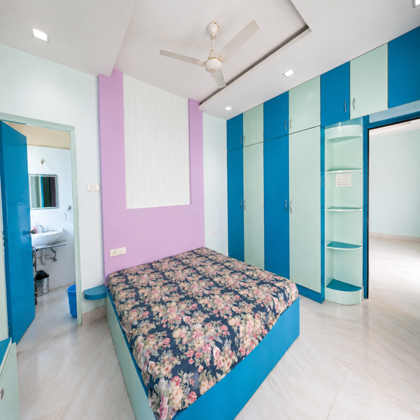 spacious master bedroom, luxury bedroom interior, contemporary sleeping room, elegant bedroom, premium bedroom design, wooden platform bed, designer bed frame, geometric bedspread, colorful bedding, walnut wood finish, custom wardrobe, built in storage, large wardrobe, sliding storage, bedroom cabinetry, wooden wall paneling, accent wall, mustard yellow wall, olive green wall, modern false ceiling, decorative ceiling beams, ceiling fan, recessed ceiling lights, marble flooring, polished floor, natural sunlight, bright bedroom, airy bedroom, large floor area, dressing table, bedroom workstation, storage drawers, bedside cabinet, window curtains, floral curtains, organized bedroom, comfortable sleeping area, private living space, upscale residence, furnished apartment, rental property, family accommodation, student accommodation, students, business professionals, working professionals, corporate housing, executive accommodation, bachelor accommodation, urban living, ready to move home.